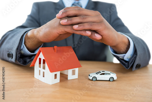 Businessman protecting house model and car with hands on table