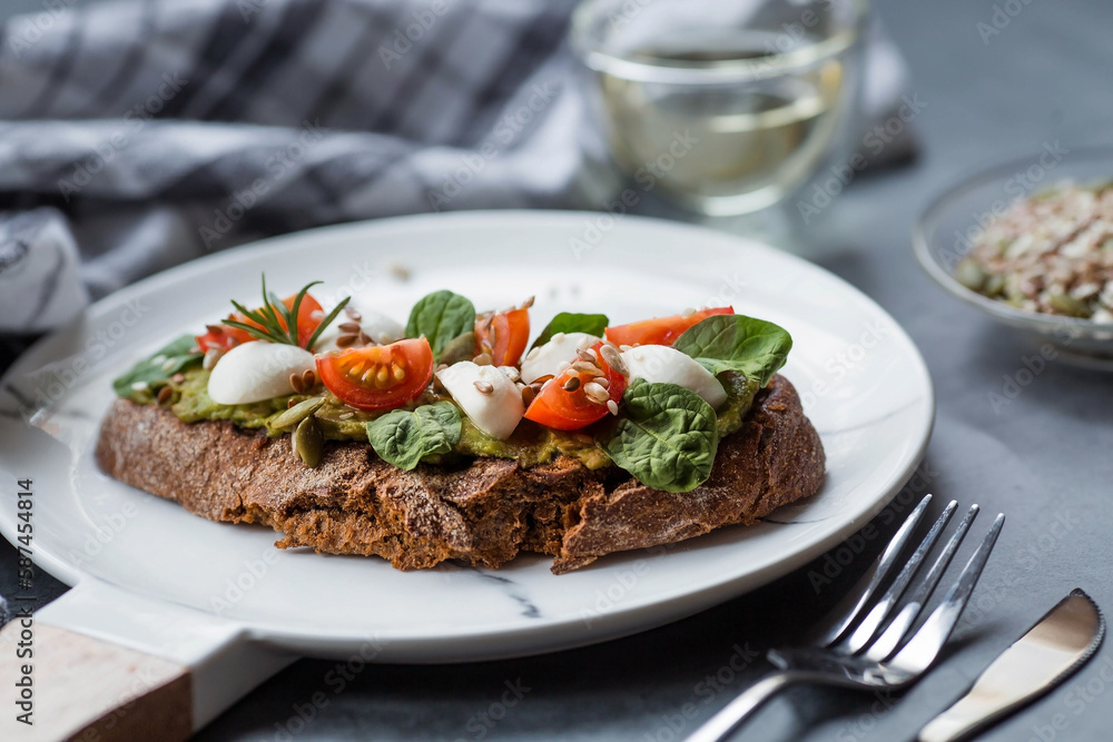 Bruschetta (sandwiches) with cherry tomatoes, mozzarella cheese and herbs on a stylish plate on a dark background. A traditional Italian snack.