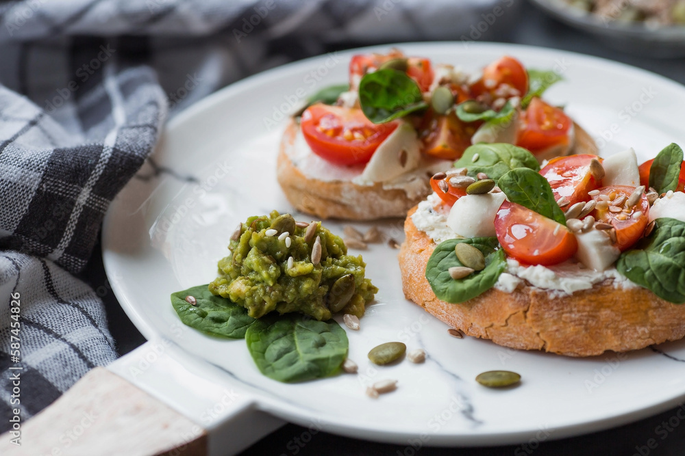 Bruschetta (sandwiches) with cherry tomatoes, mozzarella cheese and herbs on a stylish plate on a dark background. A traditional Italian snack.