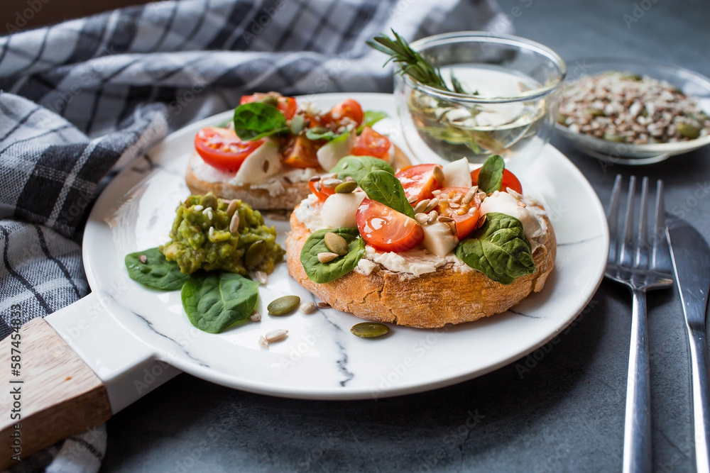 Bruschetta (sandwiches) with cherry tomatoes, mozzarella cheese and herbs on a stylish plate on a dark background. A traditional Italian snack. Bruschetta (sandwiches) with cherry tomatoes, mozzarella cheese and herbs on a stylish plate on a dark background. A traditional Italian snack.