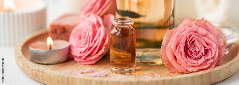 Aromatherapy. Pure organic essential rose oil concept. Elixir with plant based floral herbal ingredients. Pink flowers extract. Spa atmosphere with candle, towel. White background. Banner copy space Aromatherapy. Pure organic essential rose oil concept. Elixir with plant based floral herbal ingredients. Pink flowers extract. Spa atmosphere with candle, towel. White background. Banner copy space