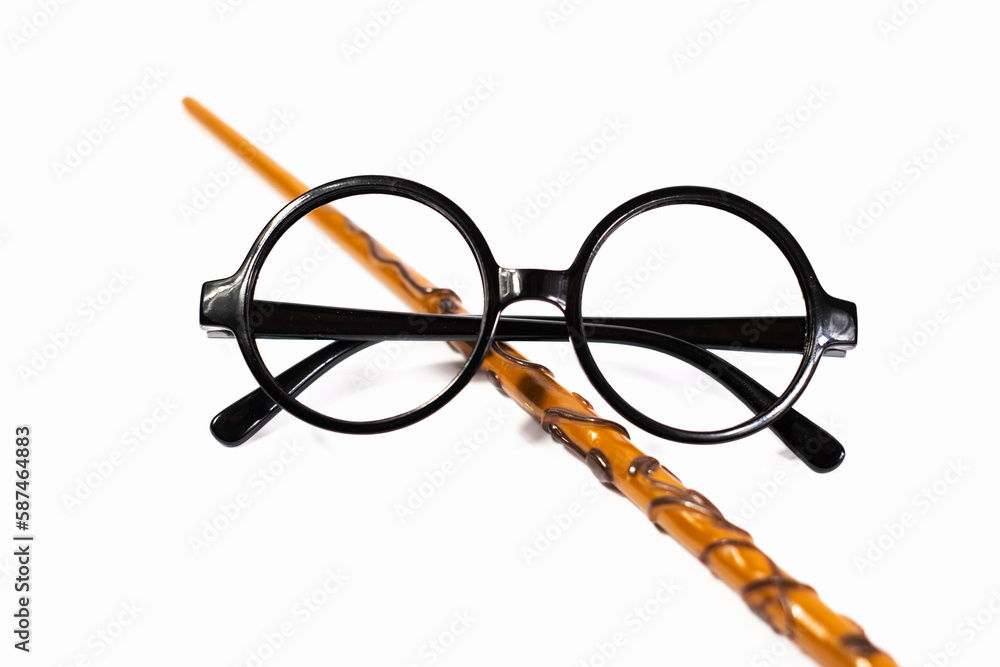 Naklejka premium Round black eyeglasses and brown magic wand isolated on white background. Harry Potter style circle glasses and wand. Wizard costume accessories. 