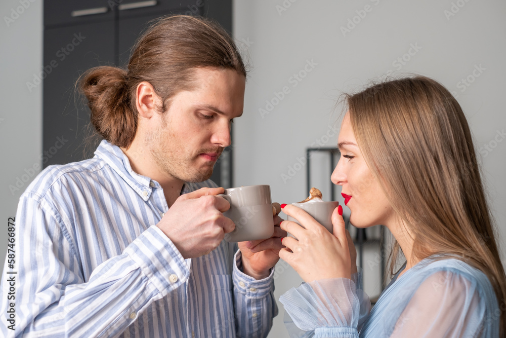 A pensive man with thick hair and a beautiful, young, smiling woman with red lips and nails, both in light blue clothes, drink coffee and watch the whipped cream in it. A pensive man with thick hair and a beautiful, young, smiling woman with red lips and nails, both in light blue clothes, drink coffee and watch the whipped cream in it.