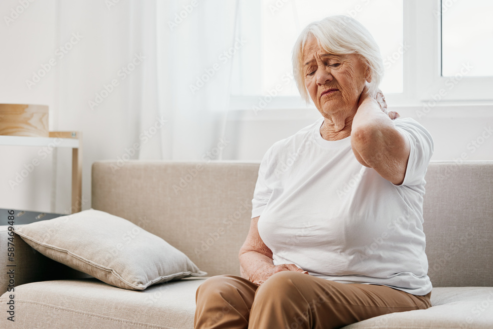 Elderly woman severe neck pain sitting on the sofa, health problems in old age, poor quality of life. Elderly woman severe neck pain sitting on the sofa, health problems in old age, poor quality of life.