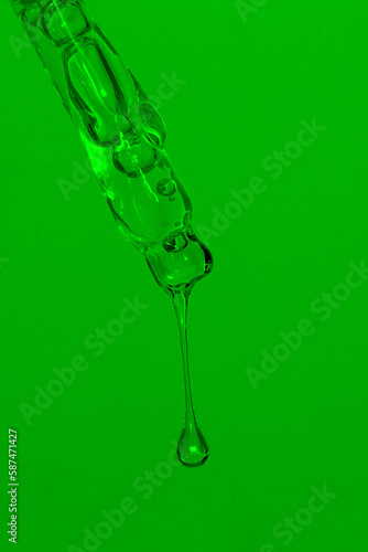 Cosmetic pipette with dripping liquid, oil and drops on a green background, serum, serum, gel, vitamin, water, oil. Natural cosmetic