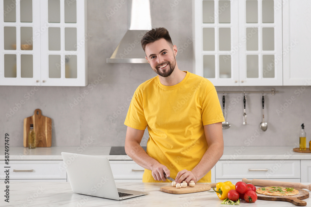 Man watching cooking online course on laptop while cutting mushrooms in kitchen. Time for hobby Man watching cooking online course on laptop while cutting mushrooms in kitchen. Time for hobby