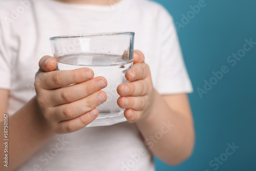 Little boy holding glass of fresh water on light blue background, closeup. Space for text