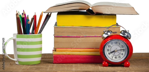 Stack of books by mug with colored pencils and alarm clock on table