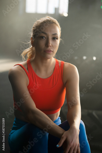 Female fitness model wearing red sportswear sitting at gym and looking at camera