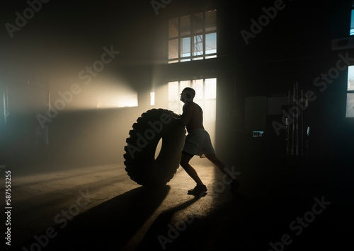 Slika na platnu Muscular shirtless man cross training with tractor tyre at the gym