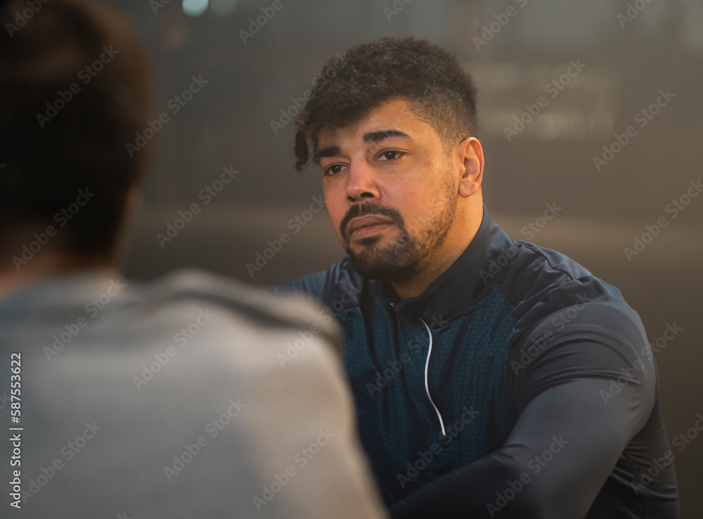 Two handsome young men sitting on floor and talking with each other after training session at gym