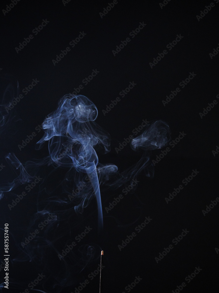 Fototapeta premium burning incense generating wisps of blue smoke on a black background