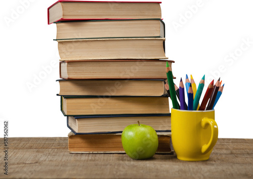 Stack of books by colored pencils in mug and apple on wooden table