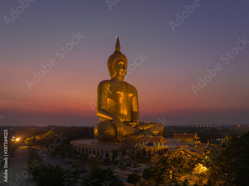 aerial view The moon was above the head of the biggest golden Buddha in the world..scenery red sky in twilight background. .golden big buddha is a popular landmark at wat Muang Ang Thong Thailand.