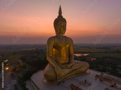 aerial view The moon was above the head of the biggest golden Buddha in the world..scenery red sky in twilight background. .golden big buddha is a popular landmark at wat Muang Ang Thong Thailand.