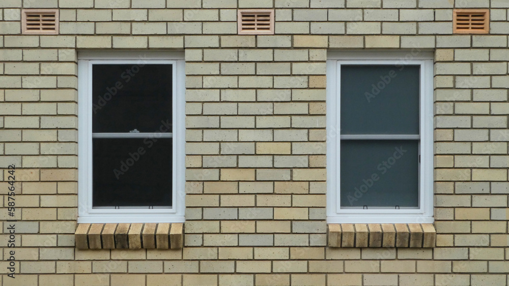 two windows with white timber frame against blonde brick wall with air vents