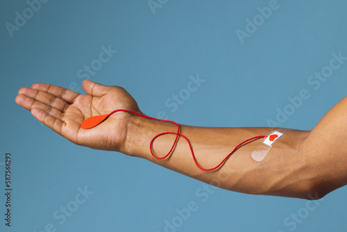 Arm of biracial man with heart sticking plaster and red string with blood drop, on blue background photo