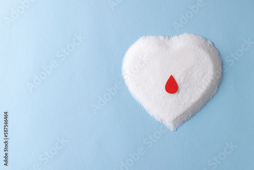 Blood drop over sugar in heart shape on blue background with copy space