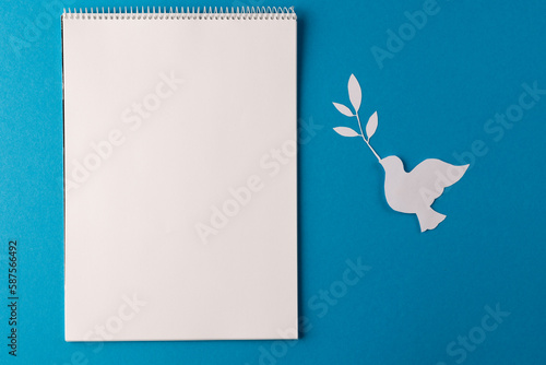 High angle view of white notebook, white dove and leaf with copy space on blue background