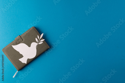 Close up of white dove with leaf over notebook and copy space on blue background