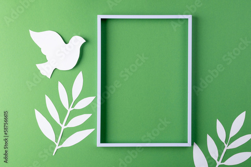 Close up of white dove and frame with leaves and copy space on green background