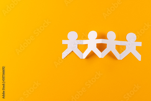 Close up of four paper cut out people figures holding hands with copy space on orange background