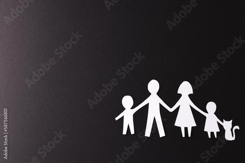 Fototapeta Naklejka Na Ścianę i Meble -  White paper cut out of family with two children and cat and copy space on black background