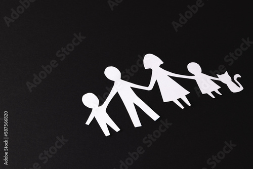 Fototapeta Naklejka Na Ścianę i Meble -  White paper cut out of family with two children and cat and copy space on black background