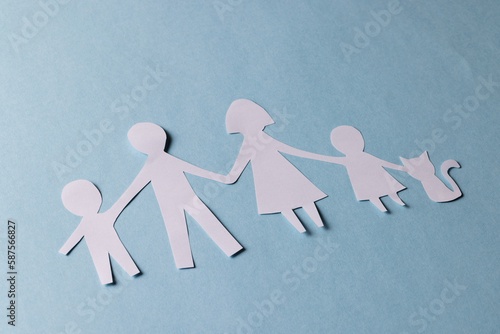 Fototapeta Naklejka Na Ścianę i Meble -  White paper cut out of family with two children and cat and copy space on blue background