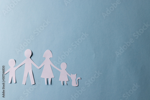 Fototapeta Naklejka Na Ścianę i Meble -  White paper cut out of family with two children and cat and copy space on blue background
