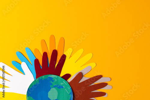 Paper cut out of multi coloured hands and globe with copy space on yellow background