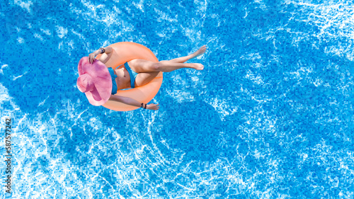 Beautiful woman in hat in swimming pool aerial drone view from above, young girl in bikini relaxes and swims on inflatable ring donut and has fun in water on tropical vacation on holiday resort 