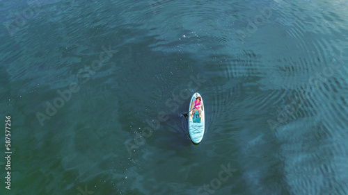 Woman paddling on SUP board on blue water, standing up paddle boarding travel, aerial drone view from above  © Iuliia Sokolovska