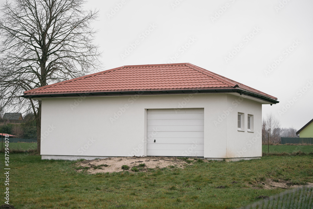 modern garage building with rolled white walls and a tiled red roof and a roller door. automobile hangar exterior with white gates. modern garage building with rolled white walls and a tiled red roof and a roller door. automobile hangar exterior with white gates.