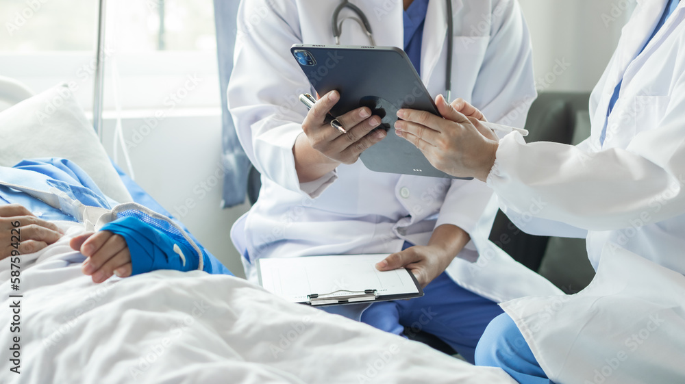 Cropped image of doctor in uniform with stethoscope using tablet standing in hospital with patient lying in bed on background Operator checks patient information on digital tablet Cropped image of doctor in uniform with stethoscope using tablet standing in hospital with patient lying in bed on background Operator checks patient information on digital tablet