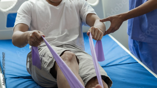 Patient stretches hands and feet at close range with flexible exercise bands and physiotherapist's hands to assist in the clinic room.