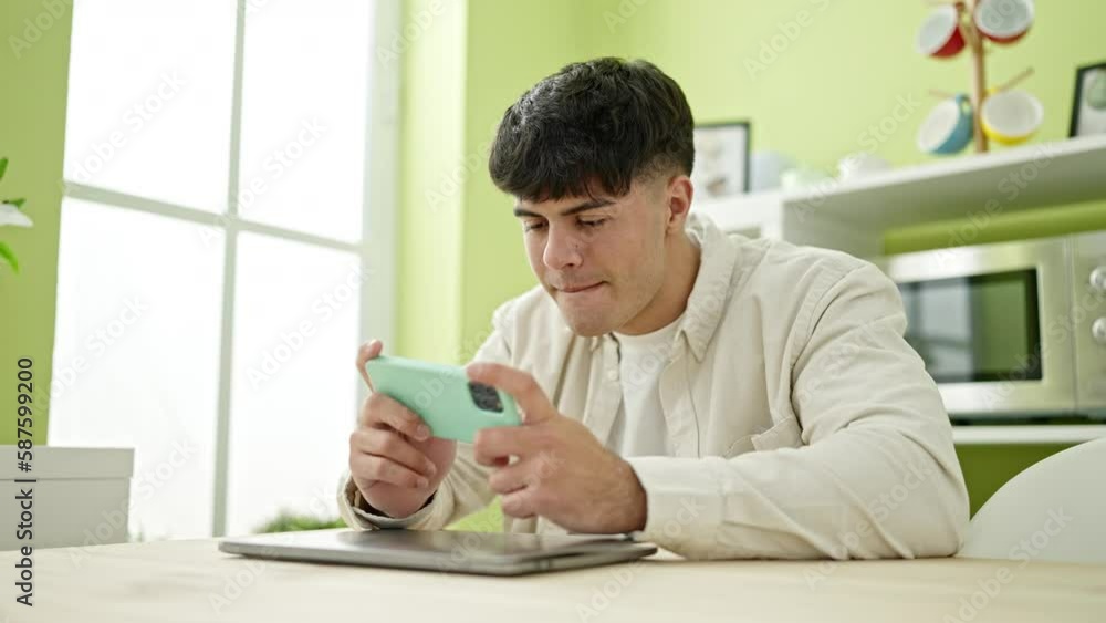 Young hispanic man playing video game sitting on table at dinning room Young hispanic man playing video game sitting on table at dinning room