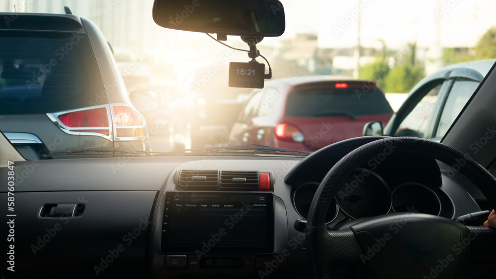Transportation driving inside car. Console car with LCD monitor. On top with camera recoder. Saw a small hand on the steering wheel of the car. background traffic jam of cars in evening time.