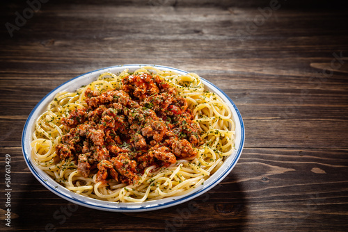 Spaghetti with minced meat, tomato sauce, parmesan cheese and seasonings served on wooden table
