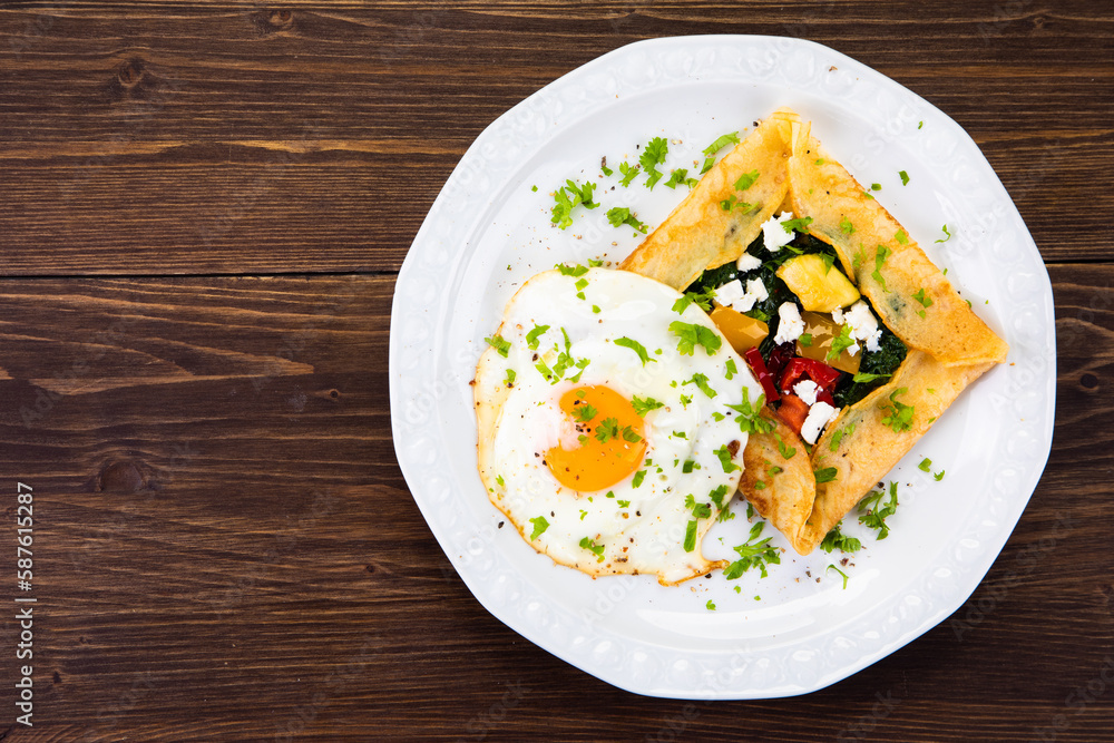Savory crepes with feta, fried vegetables and egg on wooden background Savory crepes with feta, fried vegetables and egg on wooden background