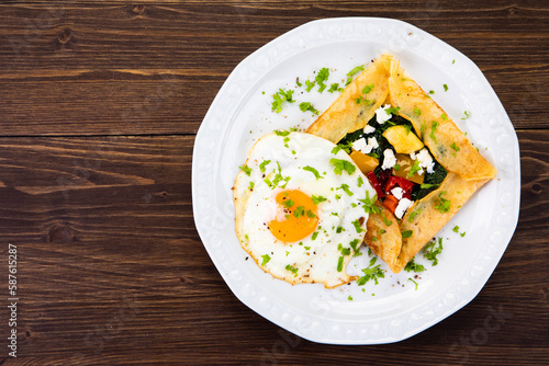 Savory crepes with feta, fried vegetables and egg on wooden background