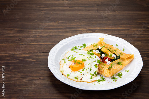 Savory crepes with feta, fried vegetables and egg on wooden background