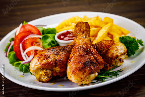 Barbecue chicken drumsticks with French fries, lettuce, tomatoes and ketchup on wooden table 
