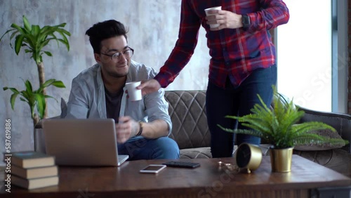 Happy same-sex couple sharing special moment of love. Lover man surprising his boyfriend brought coffee, embracing, kissing. Romantic partners sit at loft monochrome interior. photo