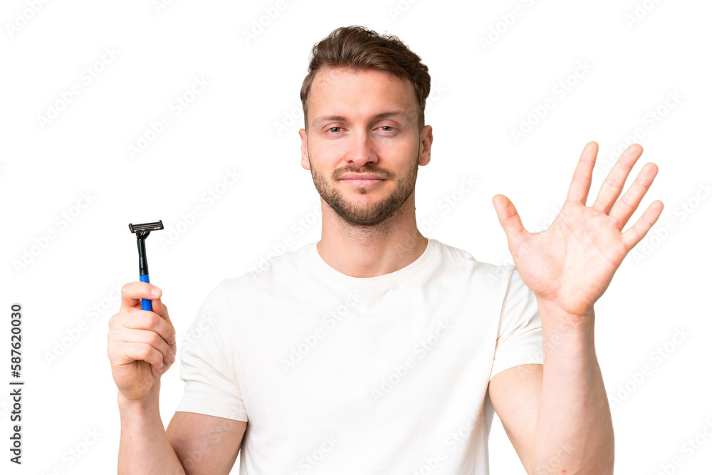 Young caucasian man shaving his beard  over isolated chroma key background saluting with hand with happy expression