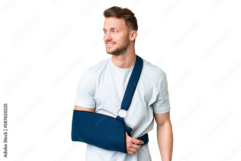 Young caucasian man with broken arm and wearing a sling over isolated chroma key background looking to the side and smiling Young caucasian man with broken arm and wearing a sling over isolated chroma key background looking to the side and smiling