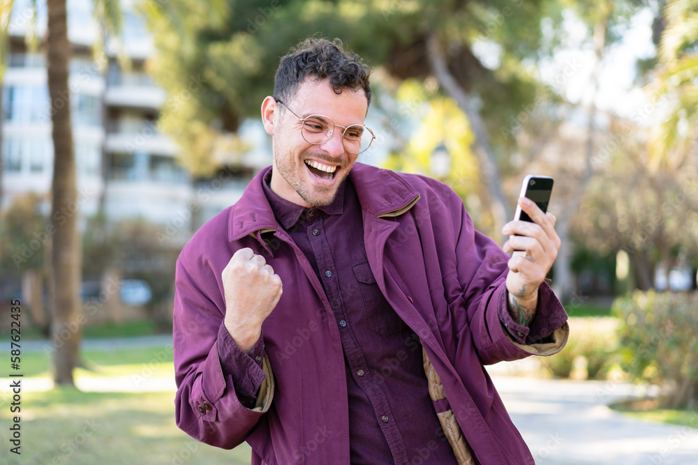 Young caucasian man at outdoors using mobile phone and doing victory gesture Young caucasian man at outdoors using mobile phone and doing victory gesture