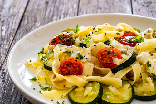 Tagliatelle with parmesan, zucchini, tomato and cream sauce on wooden table 