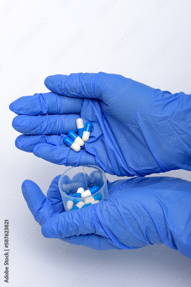 Kapsułki trzymane w dłoniach w niebieskich rękawiczkach przez pielęgniarkę - obrazy, fototapety, plakaty 