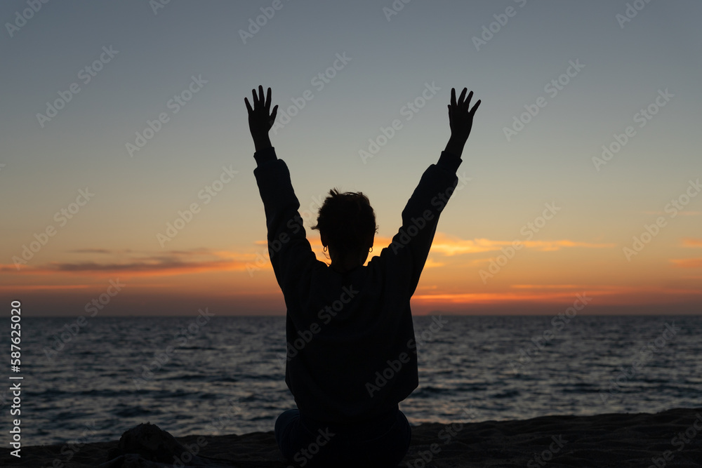 young woman backlit raising her arms in a sunset